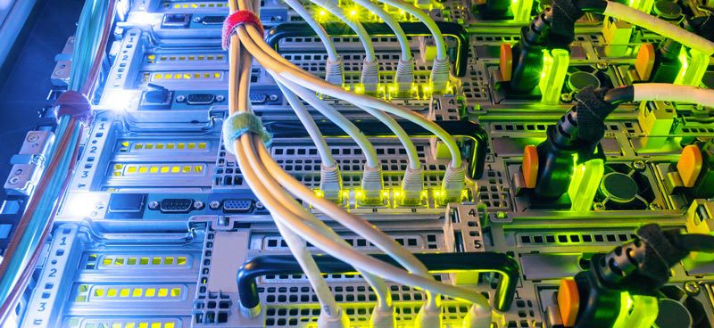 A close-up view of a server rack with multiple lit connectors and cables, featuring green and yellow lights.